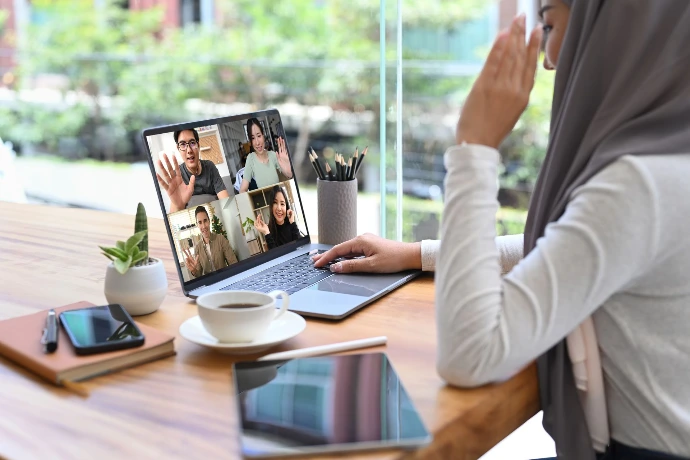 A woman sitting at a desk with garden in the background. She is talking to a group of people in an online meeting.